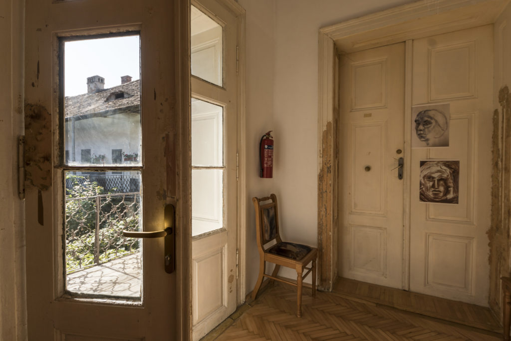 Picture of a room in an older building with two doors. One of them is leading to a terrace while the other one is closed. 